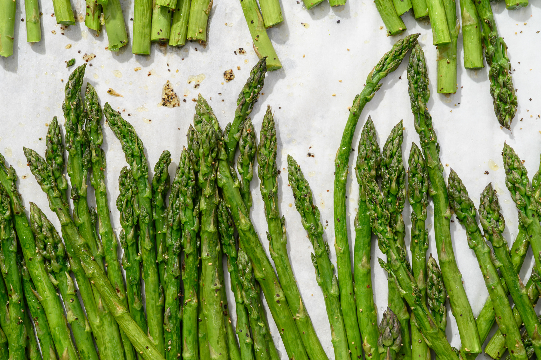 Flatlay of roasted asparagus spears with cracked pepper and olive oil on parchment paper